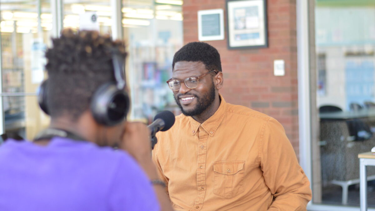 A teen wearing headphones interviewing an adult speaking into a microphone on a brown table