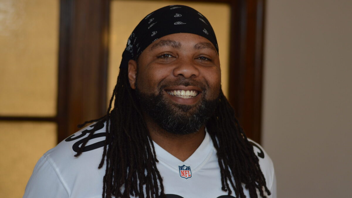 Adult with a headscarf and dreadlocks, and a short black beard and mustache smiling in profile