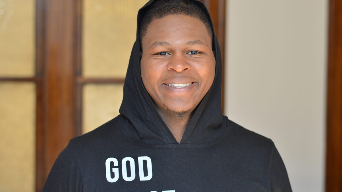 Adult with short black hair wearing a black hoodie smiling in profile
