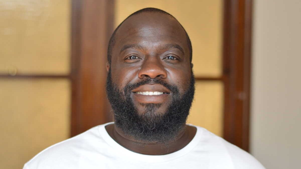 Adult with short black hair, a black beard and mustache, and a white shirt smiling in profile