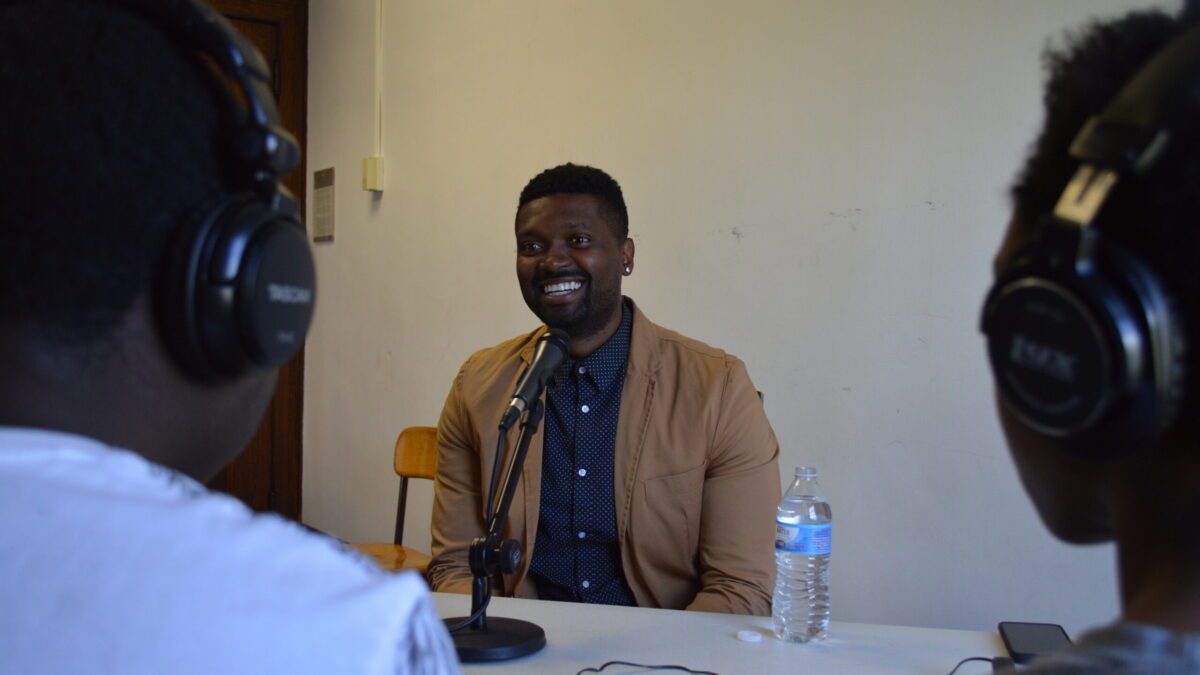 Two teens wearing headphones interviewing an adult speaking into a microphone on a white table