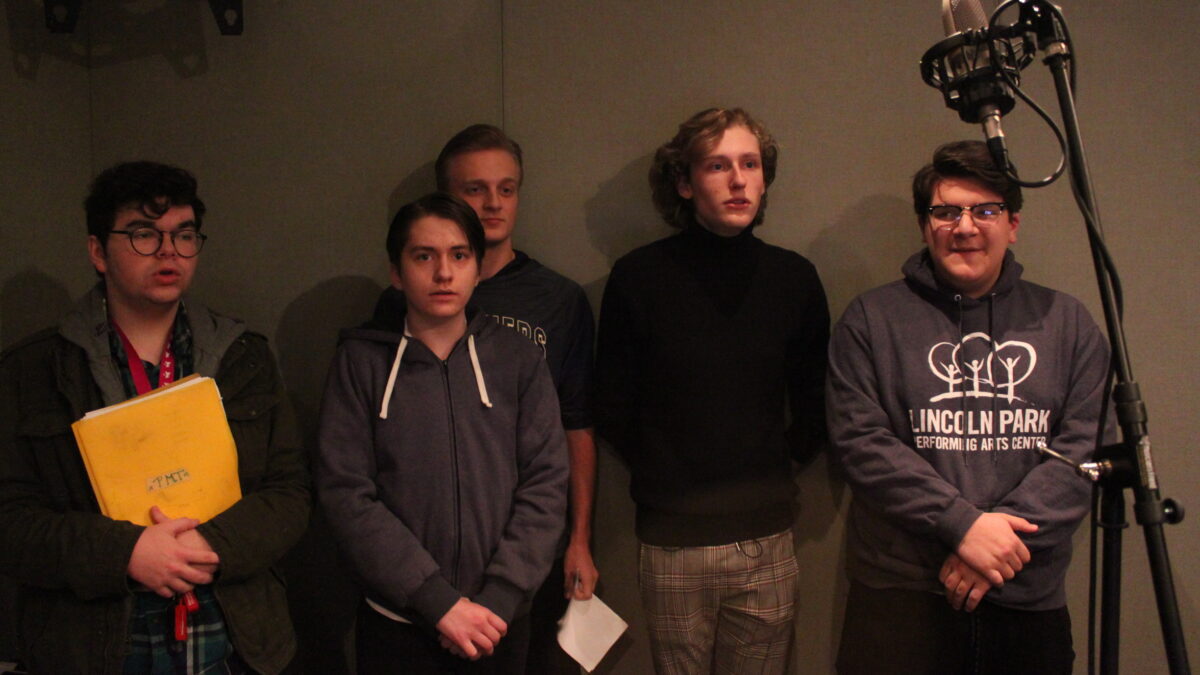 Five teens singing next to a microphone in a radio studio