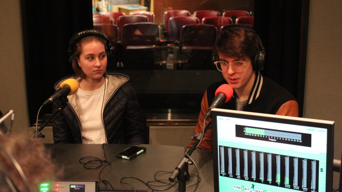 Two teens wearing headphones speaking into microphones being interviewed in a radio studio