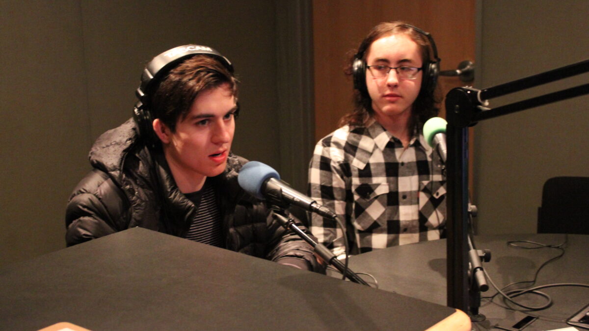 Two teens wearing headphones speaking into microphones in a radio studio