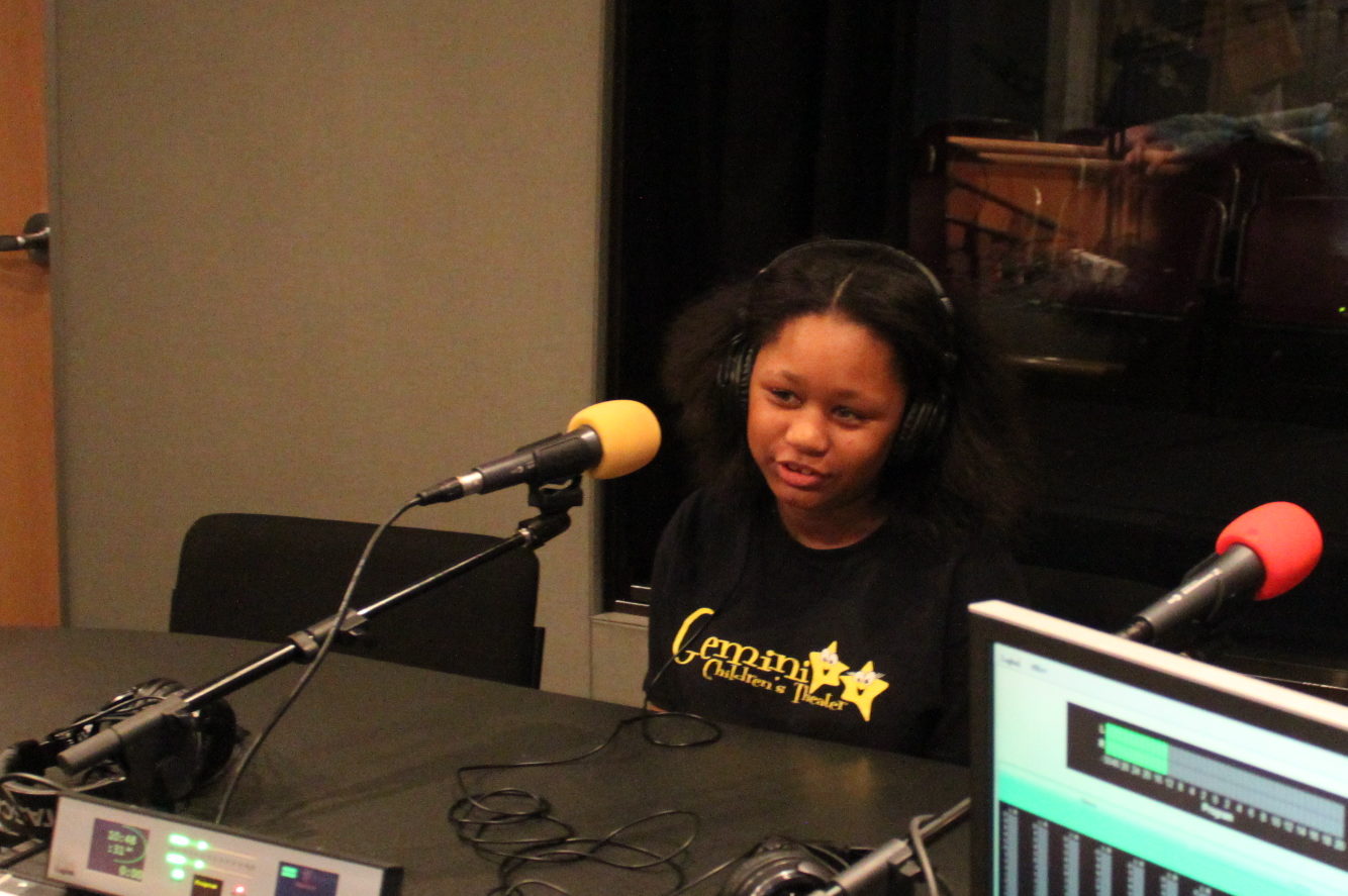 Youth wearing headphones speaking into a microphone in a radio studio