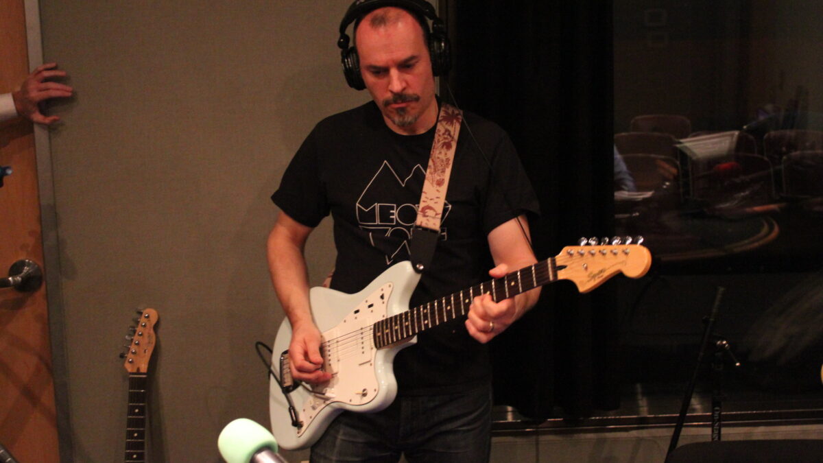 Adult wearing headphones playing guitar in a radio studio