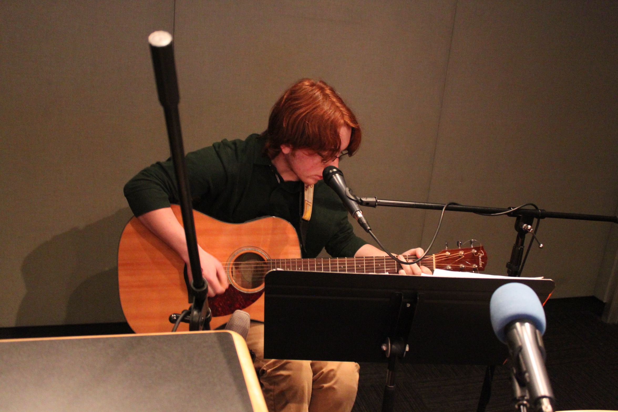 Teen playing guitar in front of a microphone and sheet music on a music stand in a radio studio
