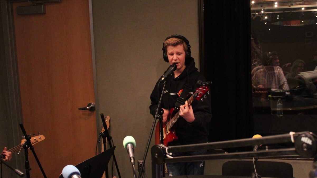 Teen wearing headphones playing guitar and singing into a microphone in a radio studio