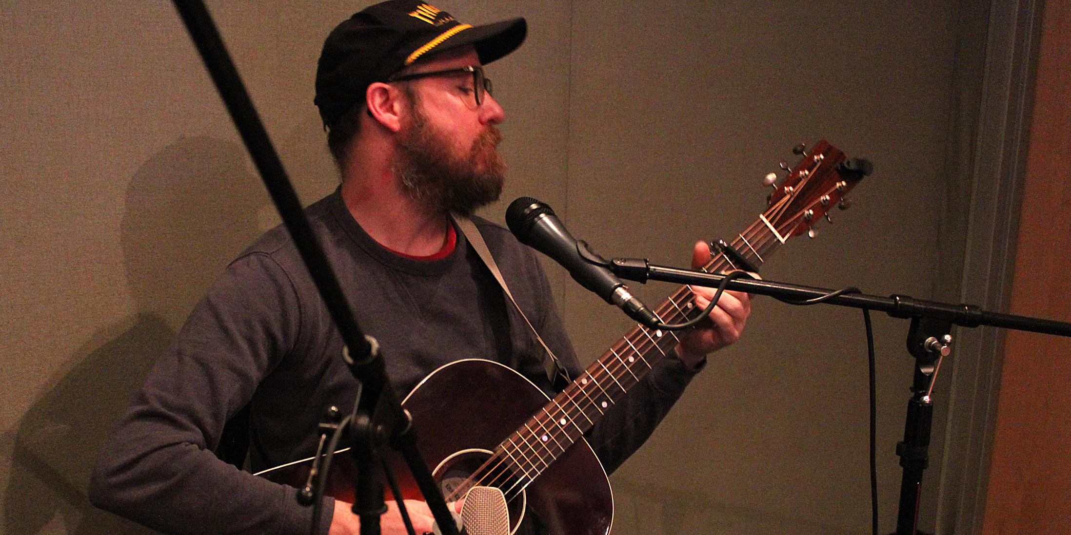 Adult playing guitar standing behind a microphone in a radio studio