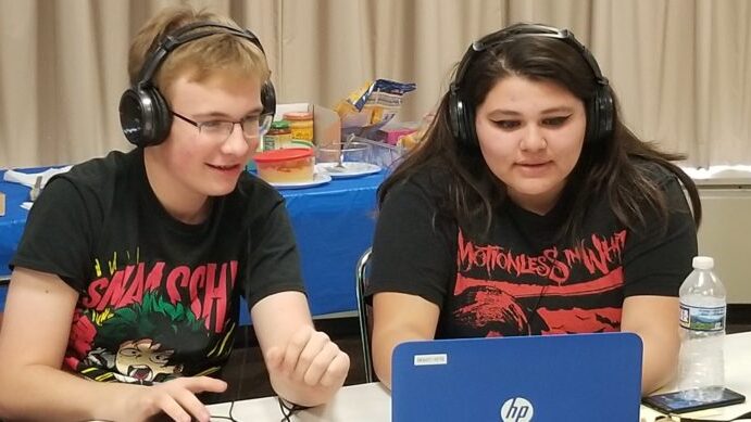 Two teens wearing headphones looking at a blue laptop