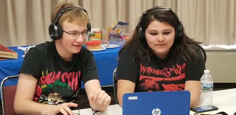 Two teens wearing headphones looking at a blue laptop