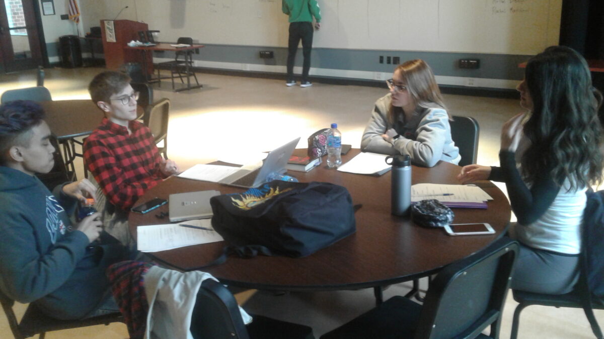Four teens having a discussion around a round wooden table