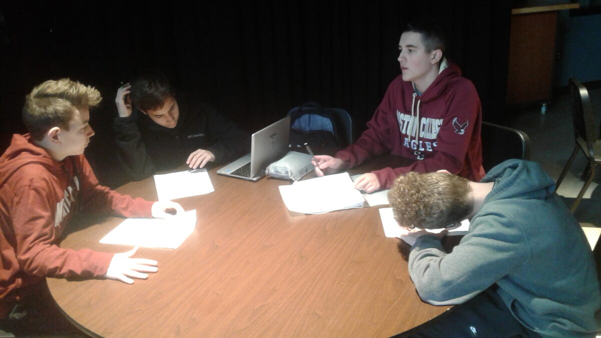 Four teens having a discussion and looking at pieces of paper on a round wooden table