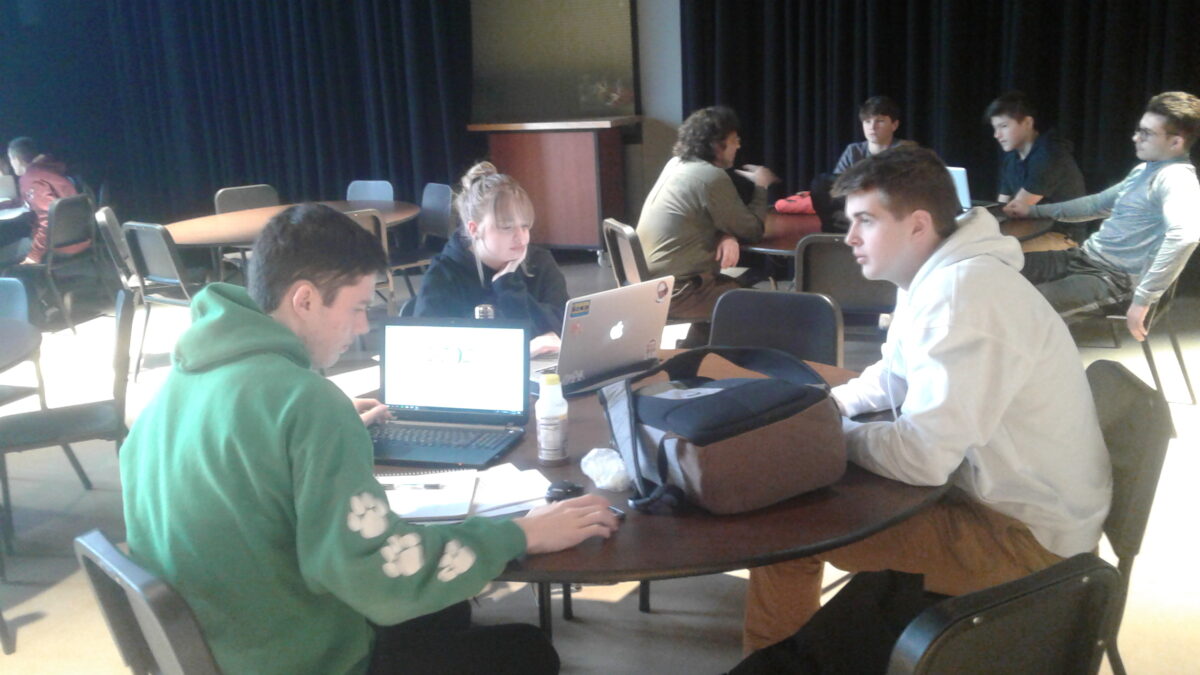 Three teens looking at laptops on a round wooden table