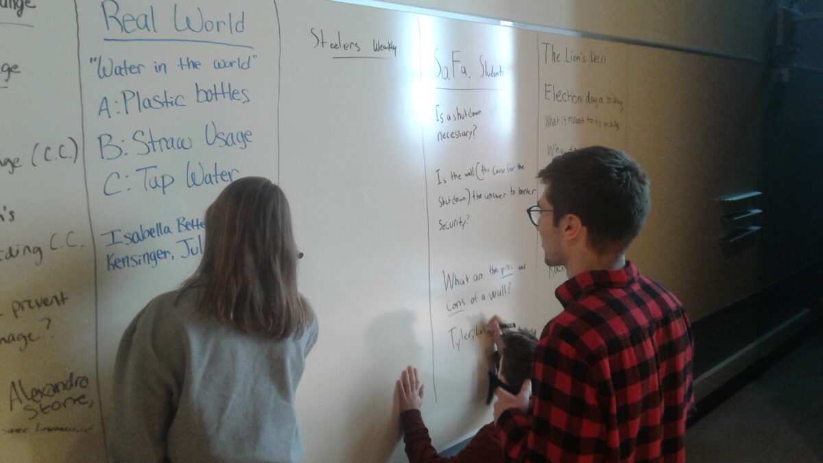 Two individuals and one child writing on a whiteboard