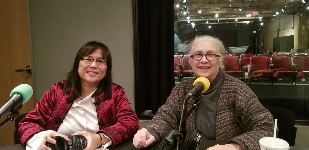 Two adults sitting behind microphones smiling in a radio studio