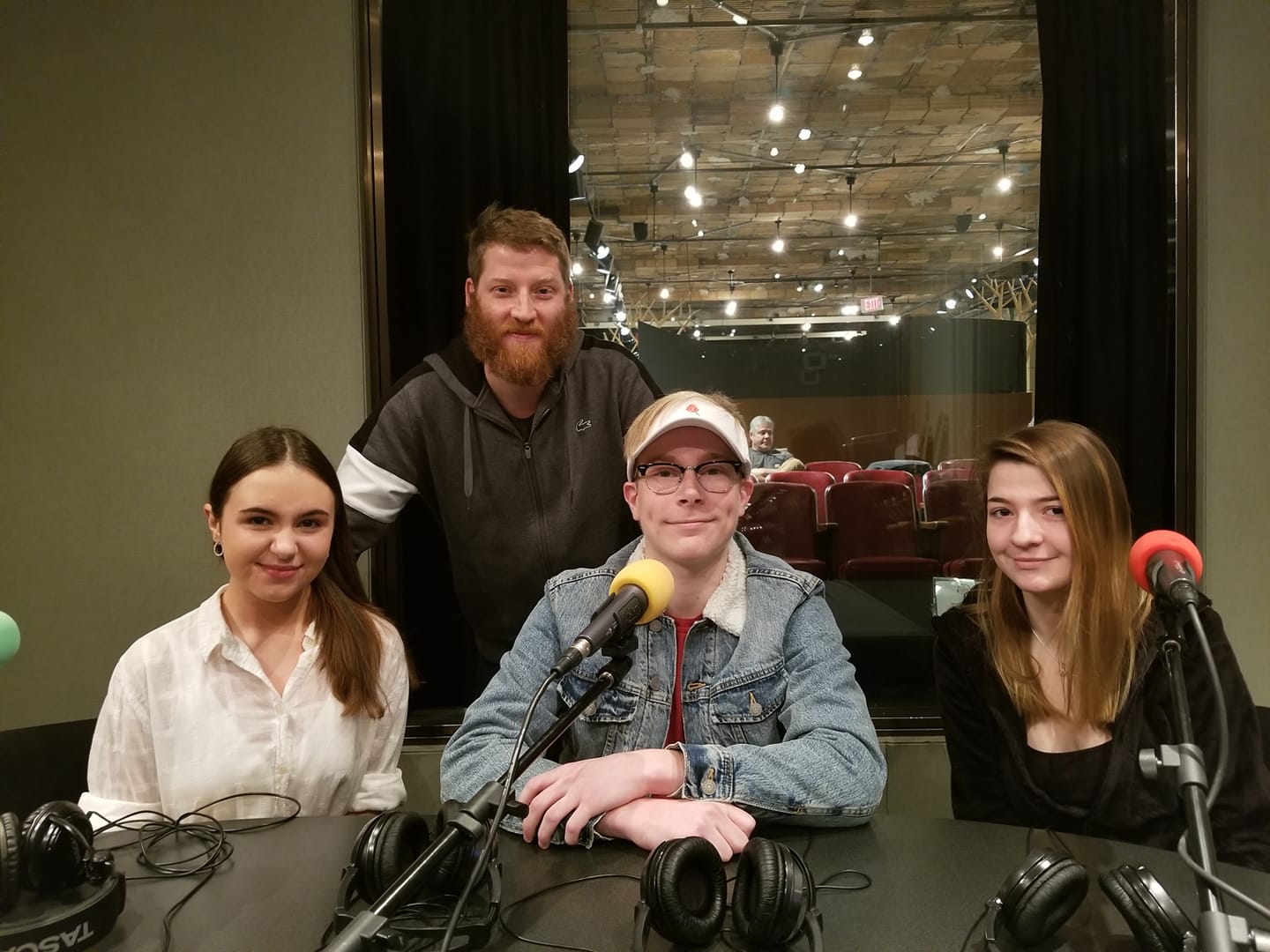 Three teens and one adult smiling and posing behind microphones in a radio studio