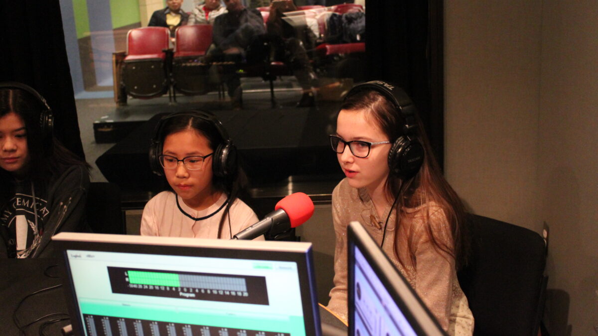 Three youth wearing headphones speaking into microphones in a radio studio