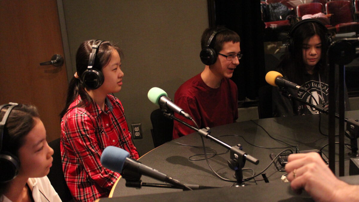 Four youth wearing headphones speaking into microphones in a radio studio