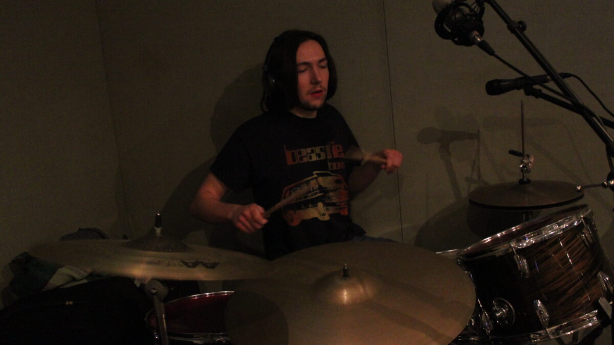 An adult wearing headphones playing drum set in a radio studio
