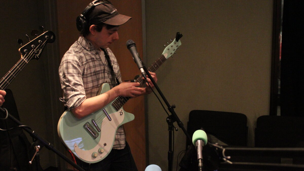 An adult wearing headphones playing guitar in a radio studio