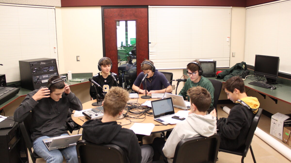 Three teens wearing headphones speaking into microphones, a teen wearing headphones looking down at a silver laptop, and three teens looking at a silver laptop on a round table
