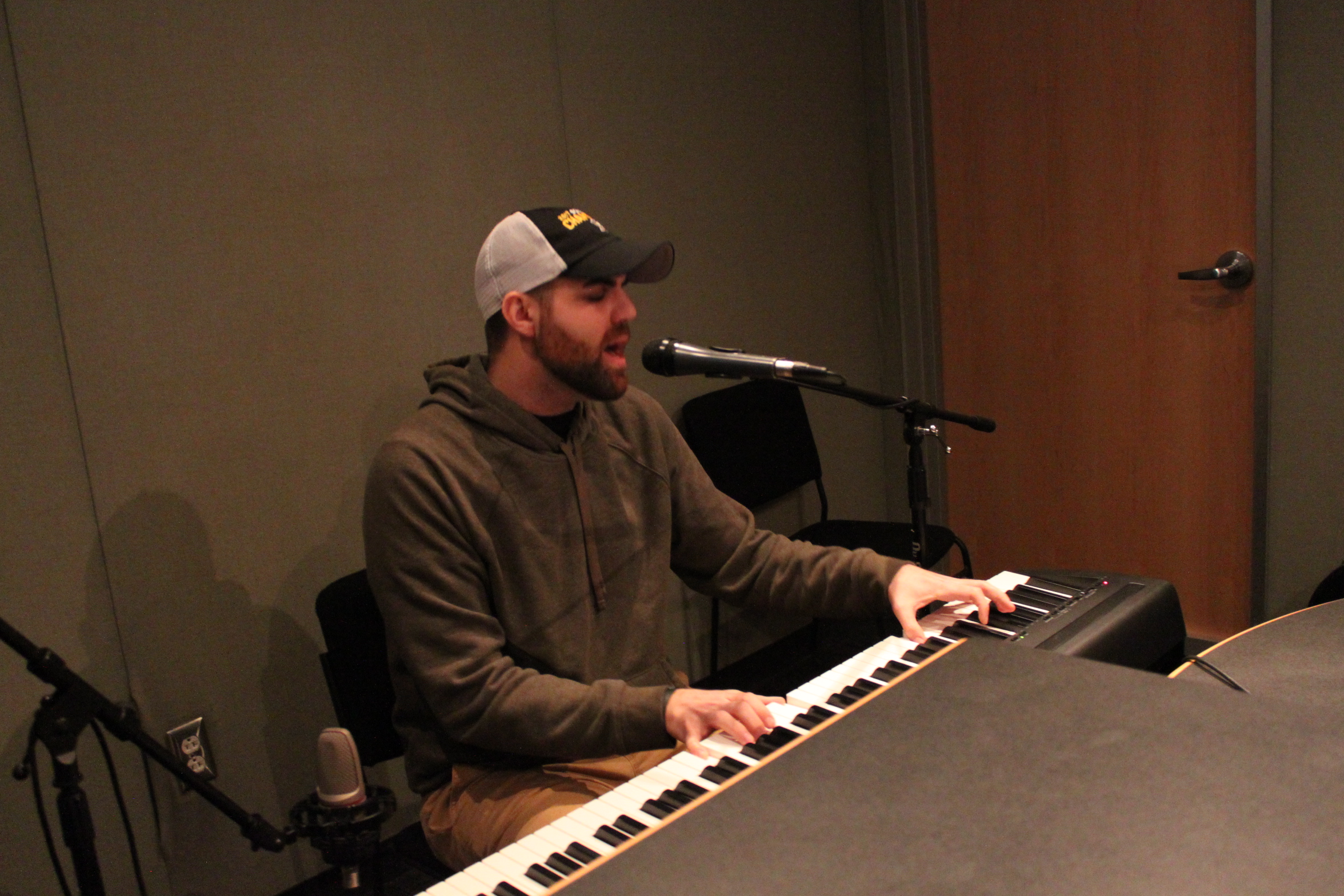 Adult playing piano keyboard and singing into a microphone in a radio studio