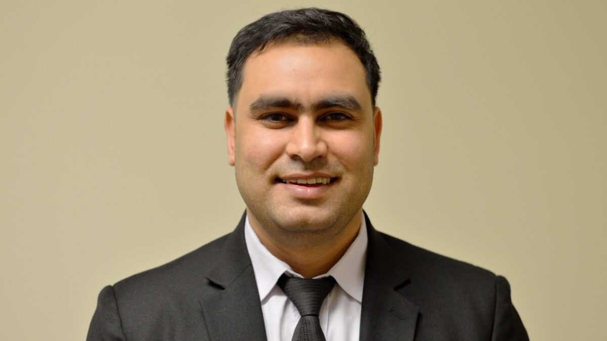 Adult with short black hair and a black suit and tie smiling in profile