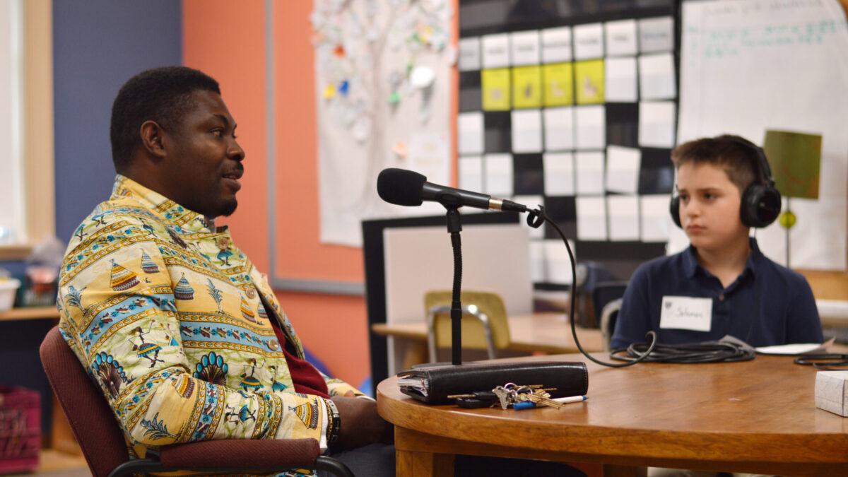 A child wearing headphones interviewing an adult speaking into a microphone in a classroom