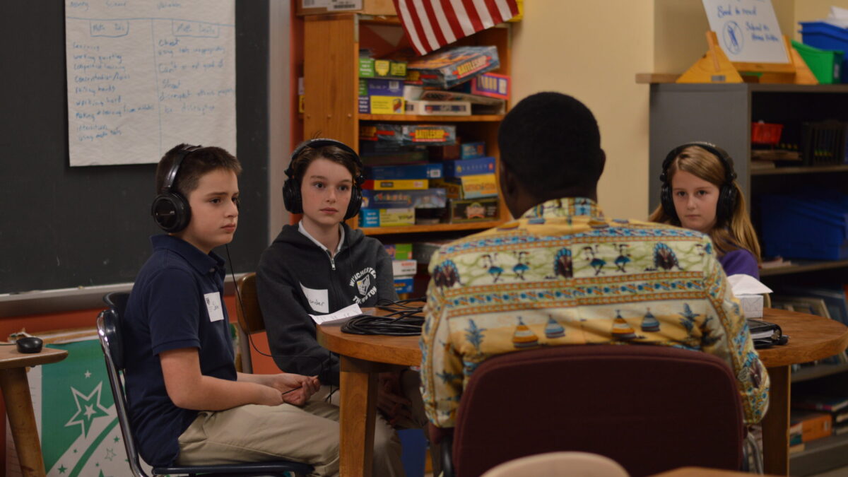 Three youth wearing headphones interviewing an adult in a classroom