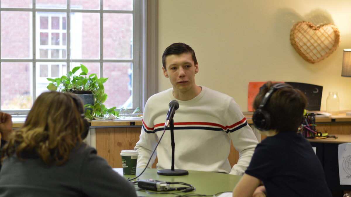 Two youth wearing headphones interviewing an adult speaking into a microphone connected to a portable recorder