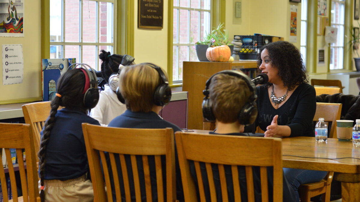 Four youth wearing headphones interviewing an adult speaking into a microphone