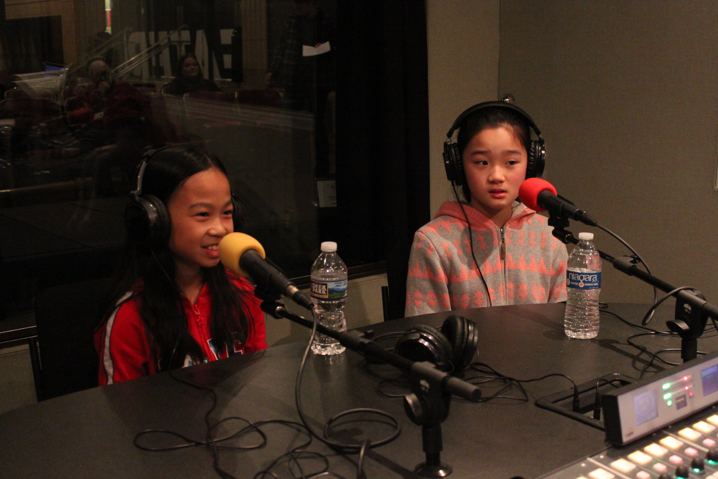 Two children wearing headphones speaking into microphones in a radio studio