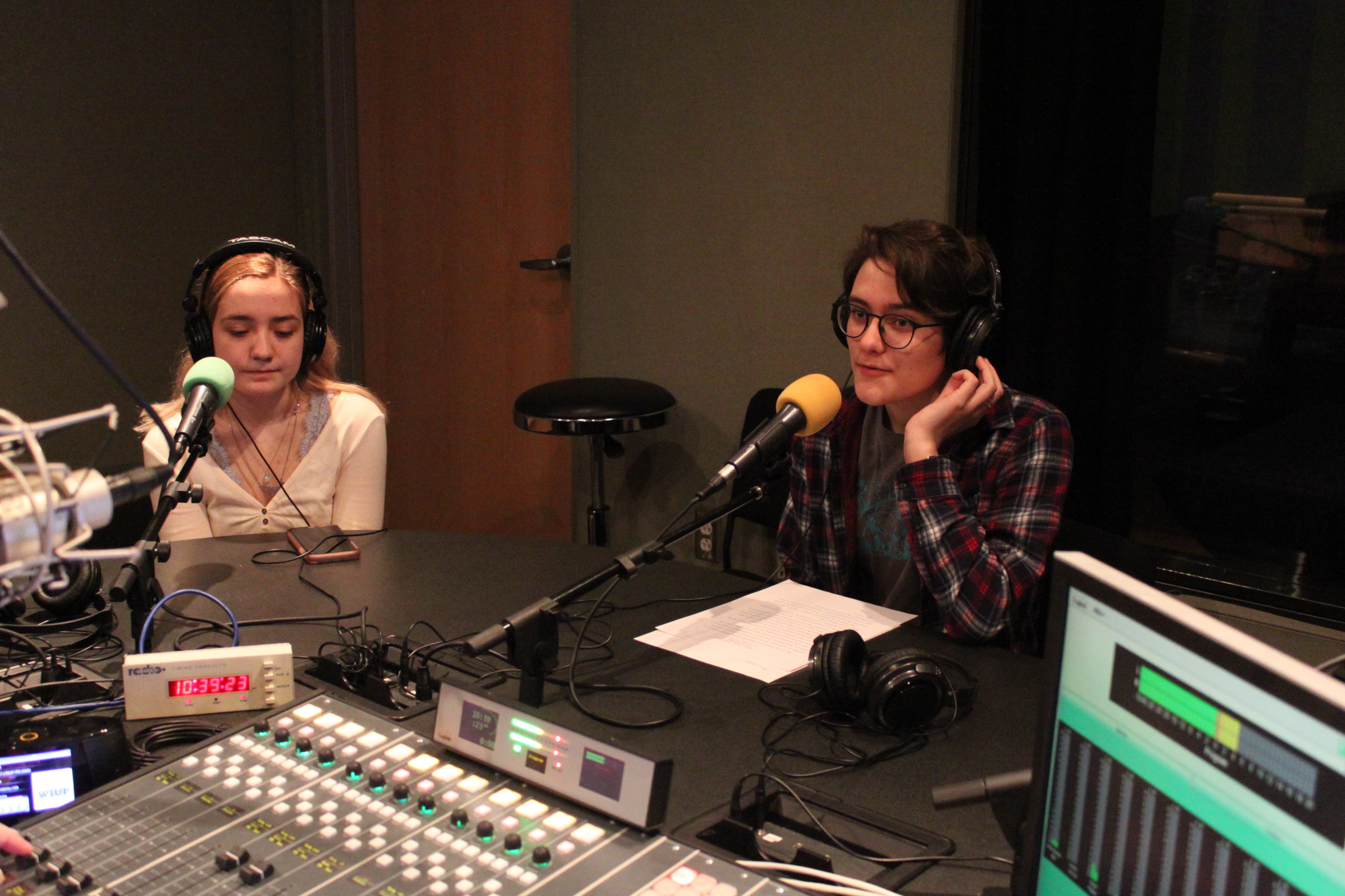 Two teens wearing headphones speaking into microphones in a radio studio