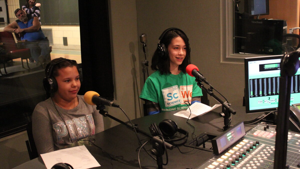 Two youth wearing headphones and speaking into microphones in a radio studio