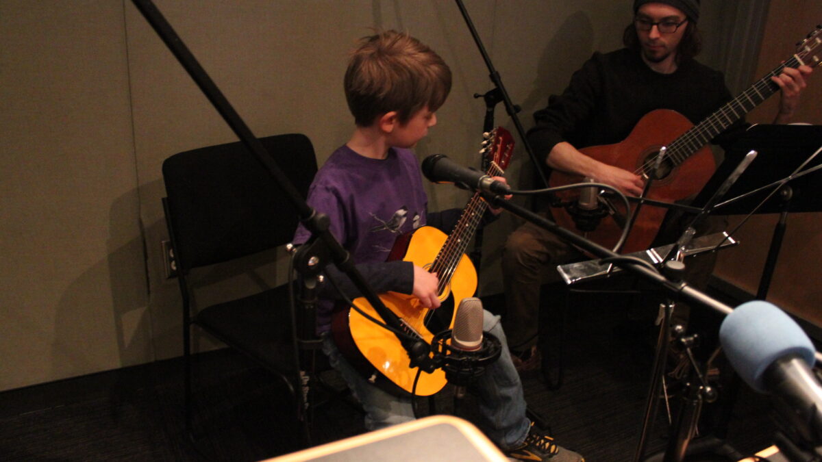 An adult and a youth playing guitar in a radio studio