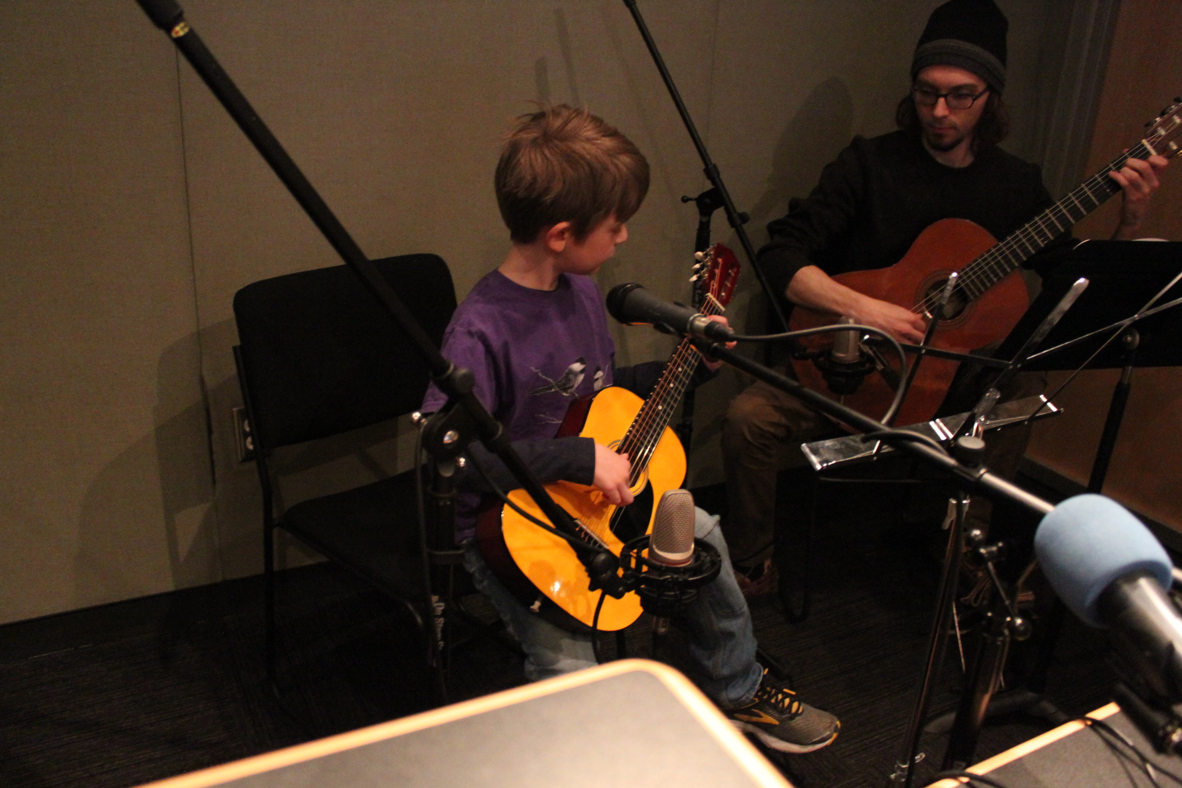 An adult and a youth playing guitar in a radio studio