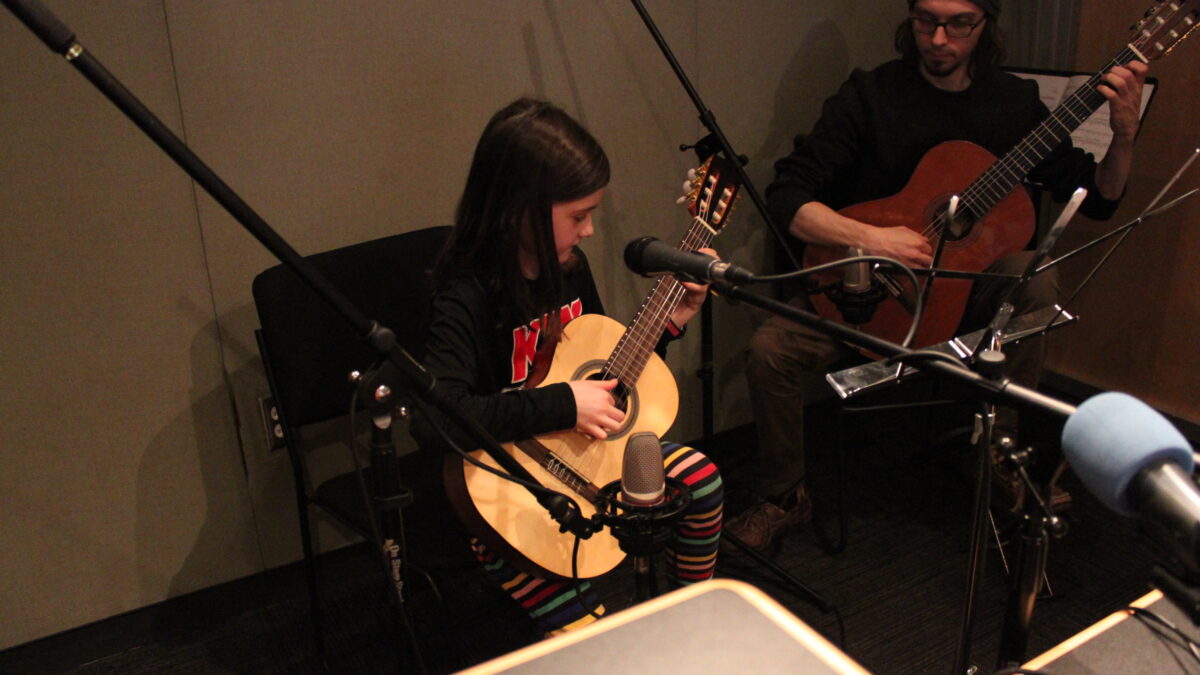 An adult and a youth playing guitar in a radio studio
