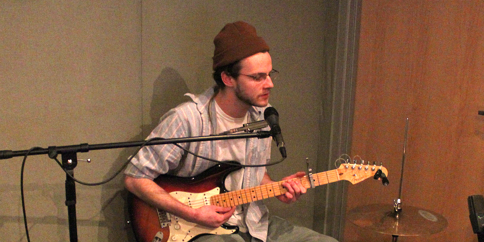 Adult playing guitar and singing into a microphone in a radio studio