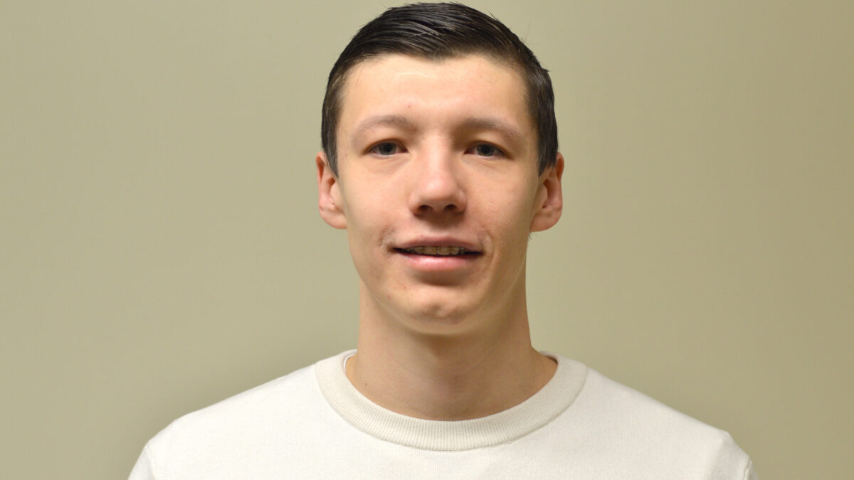 An adult with short brown hair and a white sweater smiling in profile