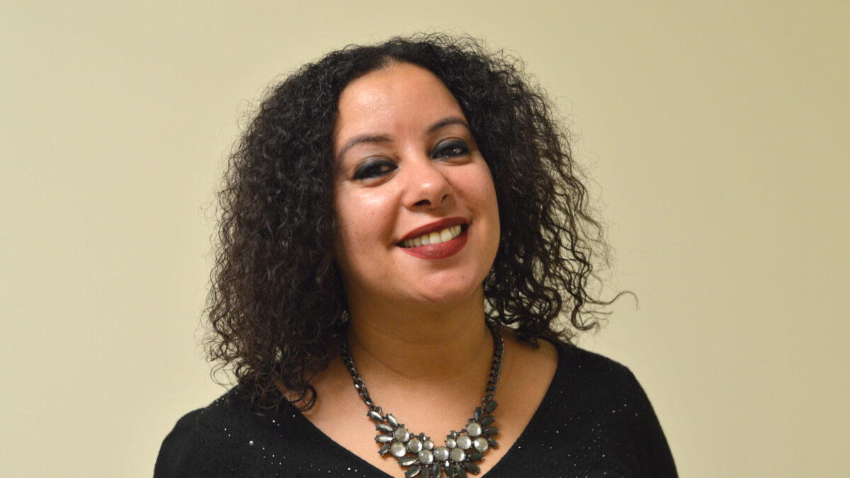 Adult with curly dark brown hair and an elaborate pearl necklace smiling in profile