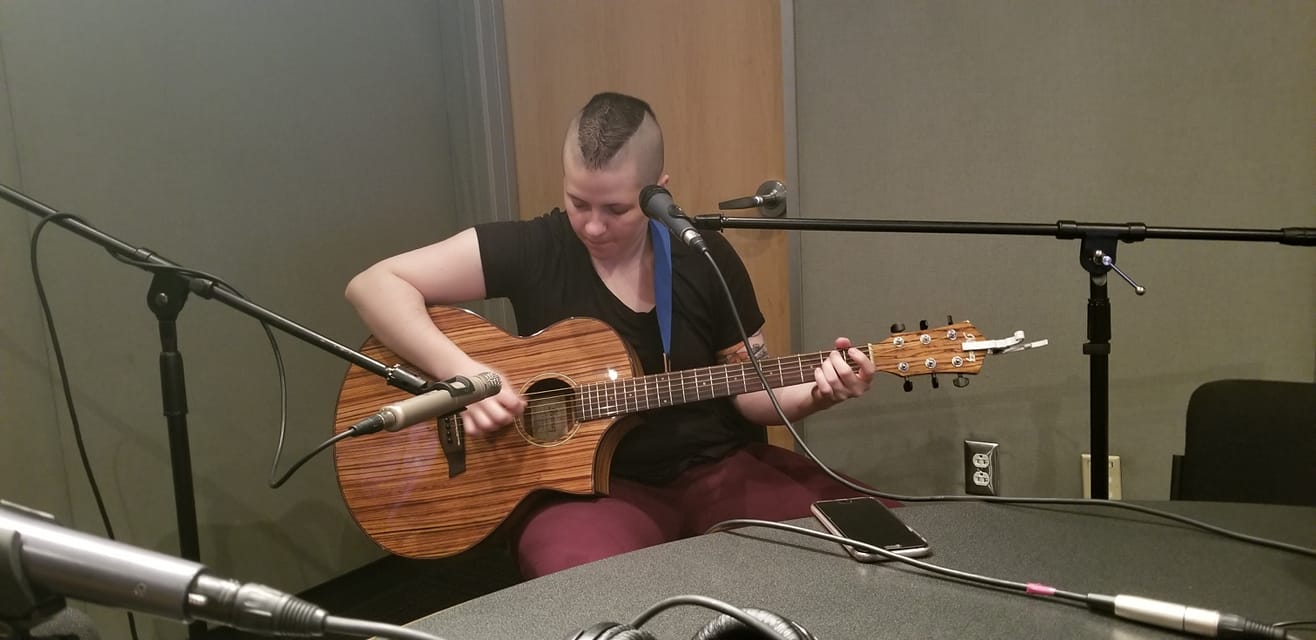 Teen playing guitar sitting behind a microphone in a radio studio