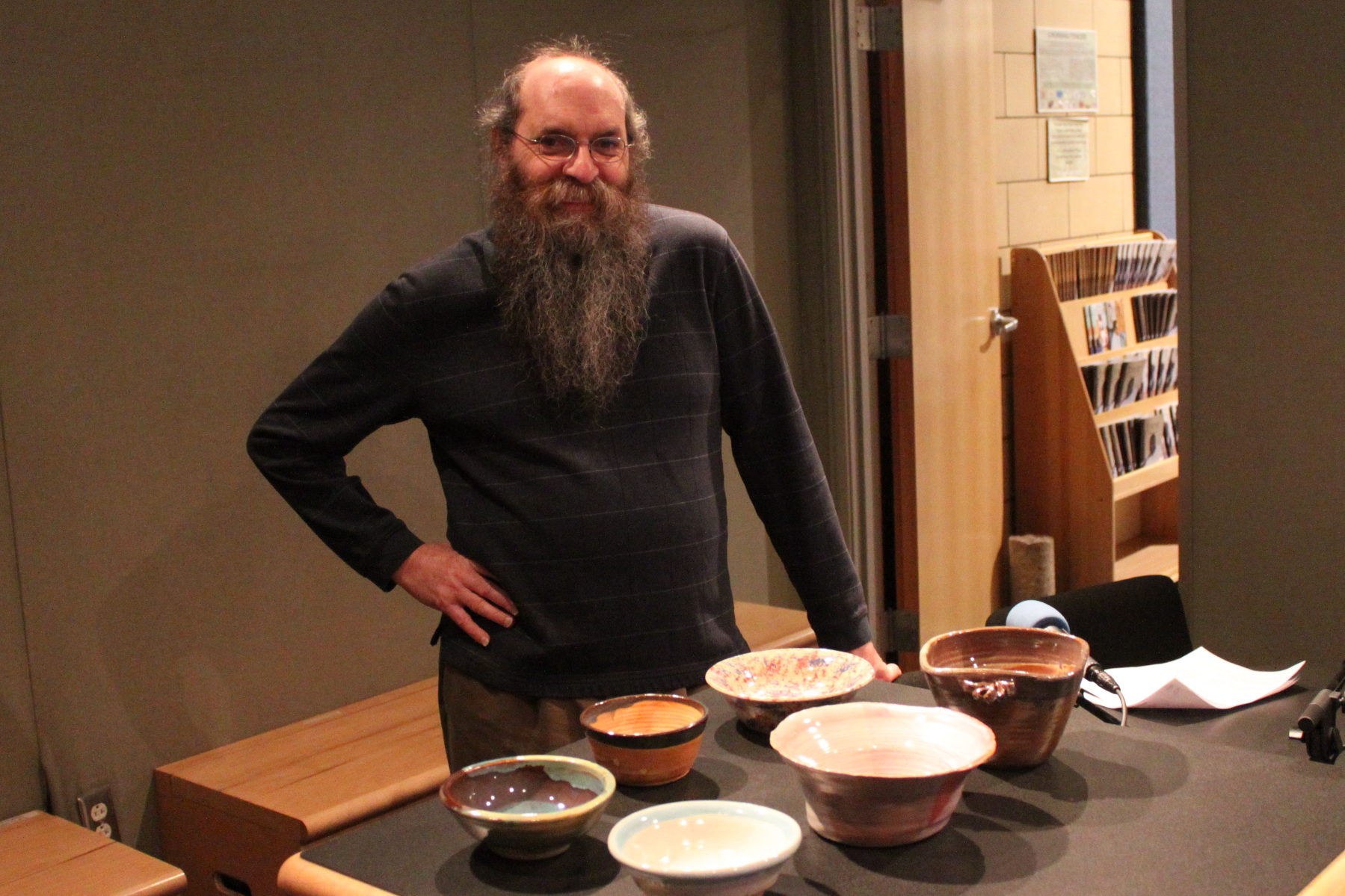 Adult posing in front of six clay bowls in a radio studio