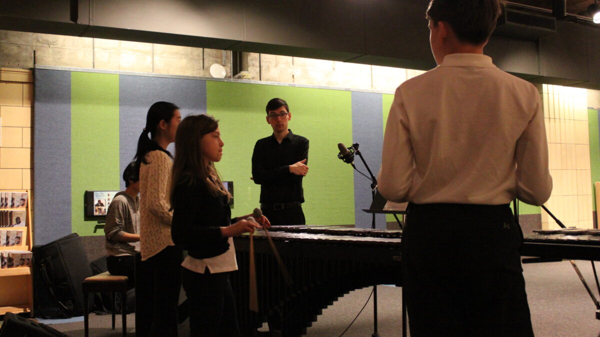 Four youth performing on xylophone, marimba, and piano keyboard as an adult looks on