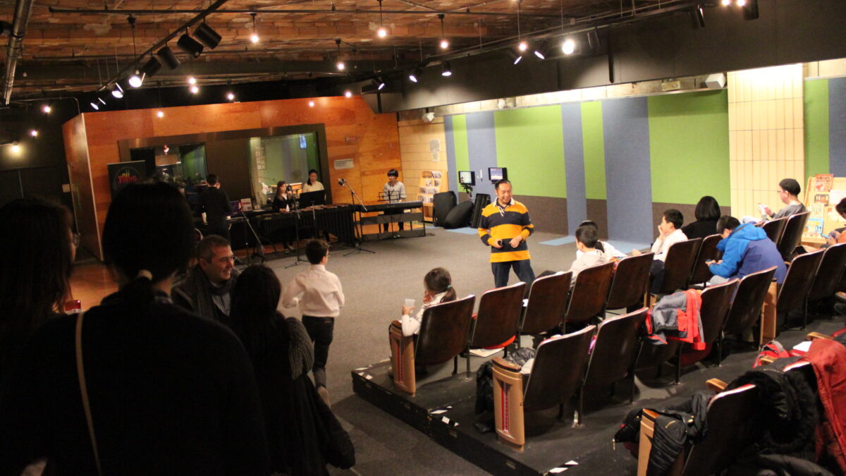 Three youth performing on piano keyboard and marimba while an audience of adults watch