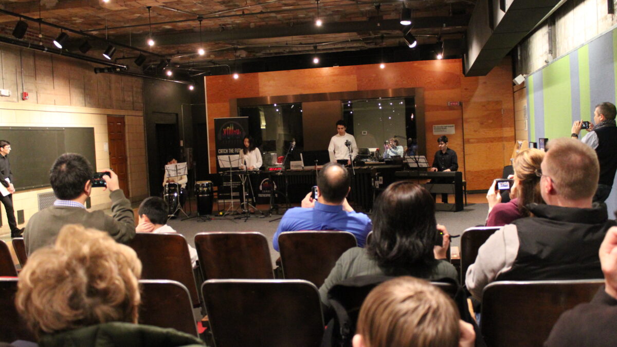 Teens playing congas, xylophone, marimba, and piano keyboard for an audience of adults