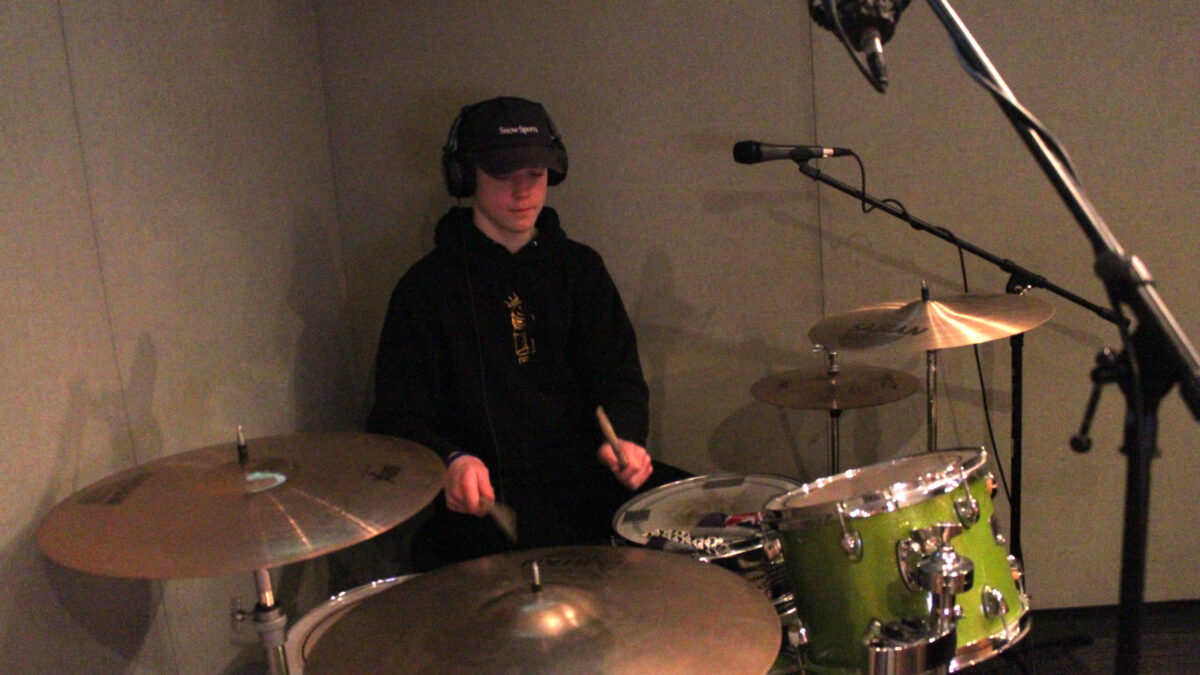 Teen wearing headphones playing a drum set in a radio studio