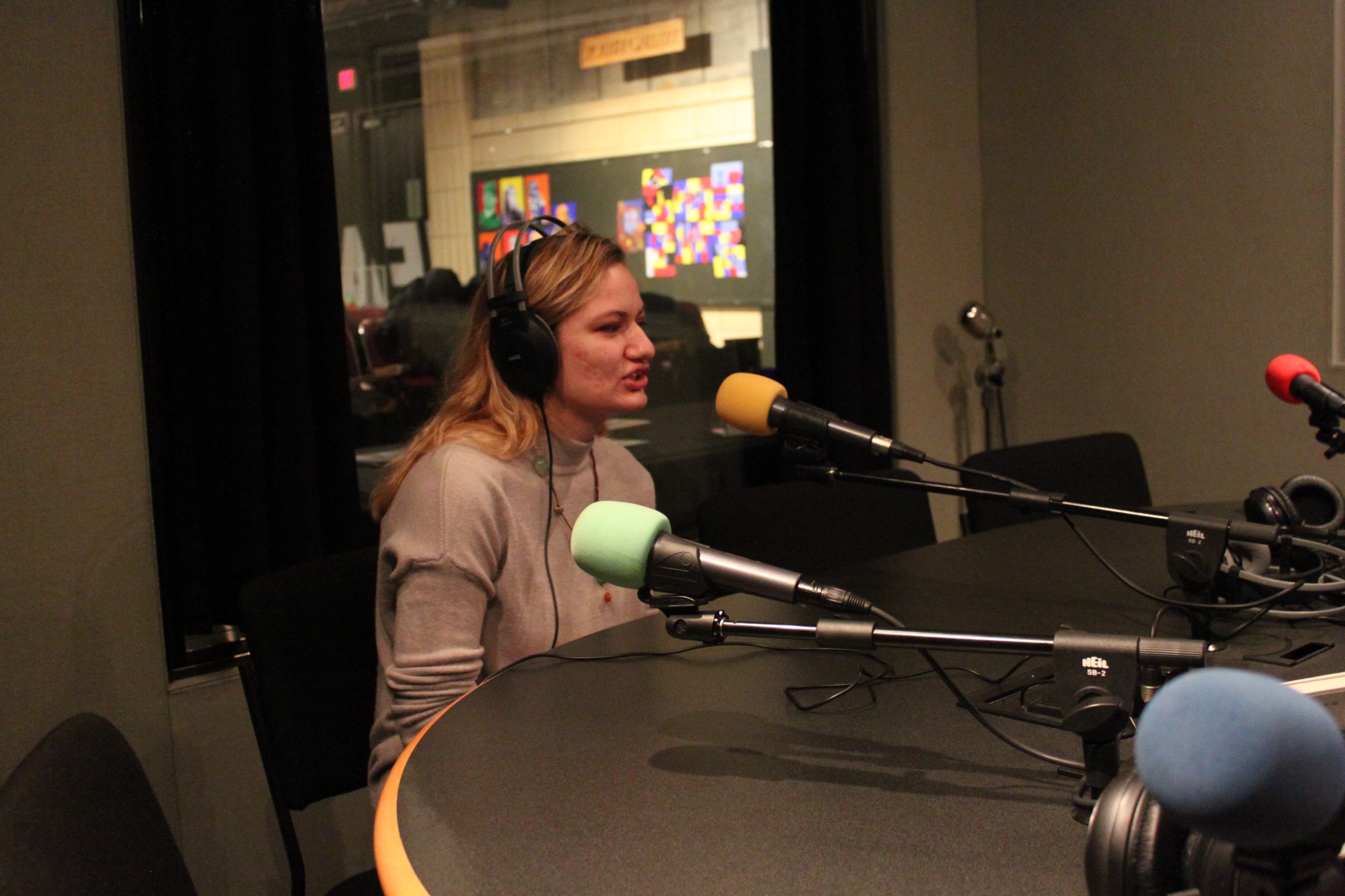 Adult wearing headphones speaking into a microphone in a radio studio