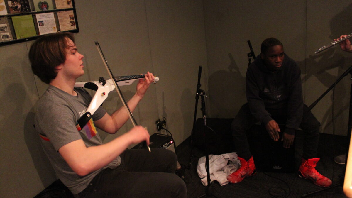A teen playing electric violin and a teen playing djembe in a radio studio