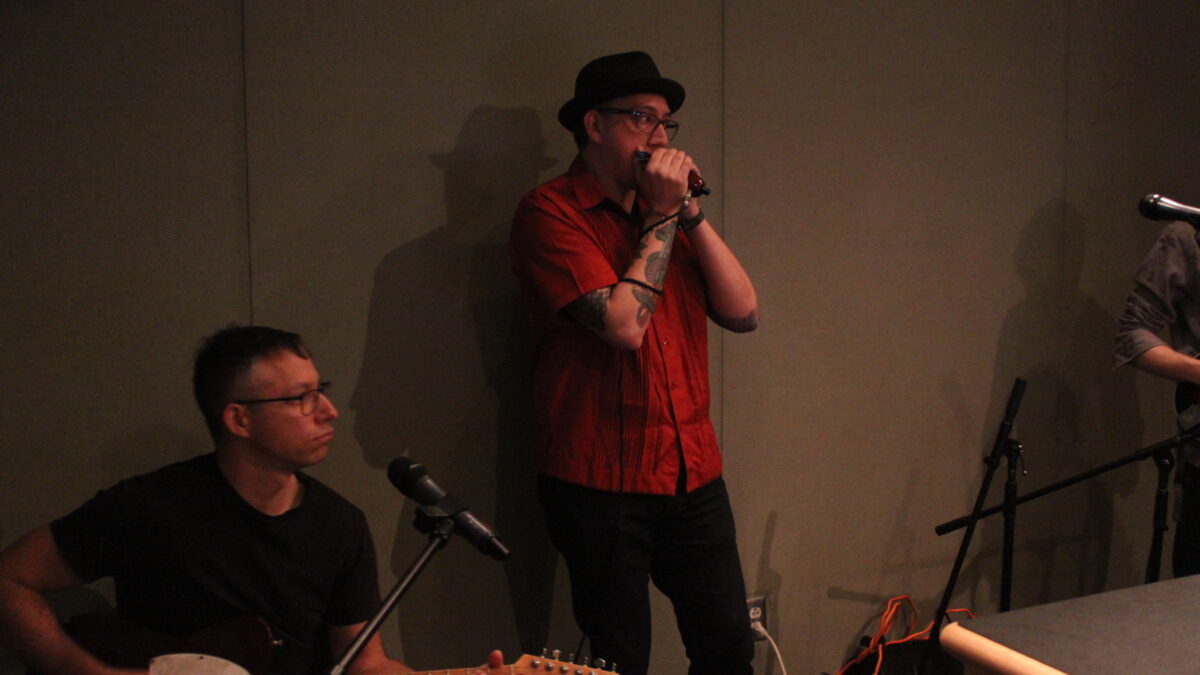An adult playing guitar and an adult playing harmonica in a radio studio